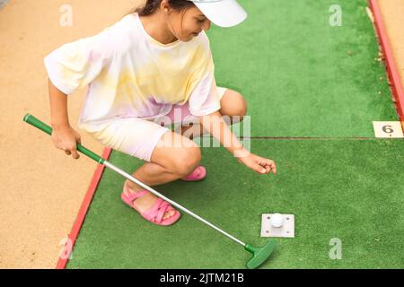 Nettes Mädchen im Vorschulalter, das mit der Familie Minigolf spielt. Glückliches Kind, das Spaß mit Aktivitäten im Freien hat. Sommersport für Kinder und Erwachsene, im Freien Stockfoto