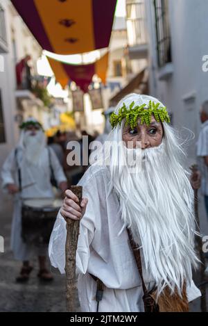 Frigiliana, Malaga, Spanien, 27. August 2022: Druide, weiß gekleidet, mit einem Baumzweig wie ein Stock, mit einem Haarreif aus grünen Blättern in den Straßen von Frig Stockfoto