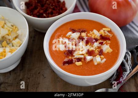 Traditionelle spanische Salmorejo-Suppe aus Tomaten, Brot, Knoblauch und Olivenöl, serviert mit gekochtem Ei und serrano-Schinken Stockfoto