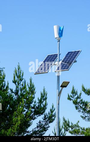 Stange mit innovativer LED-Straßenleuchte, die von Solarzellen und kleinem vertikalen Windgenerator mit blauem Himmel-Hintergrund angetrieben wird Stockfoto