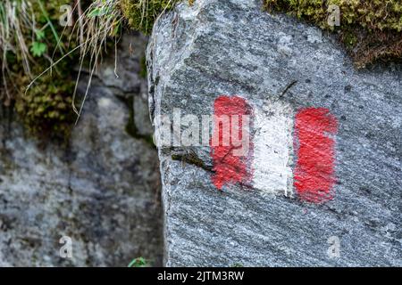 Alpenwanderweg in Österreich, markiert mit gemalter österreichischer Flagge auf einem festen Felsen entlang der Route Stockfoto