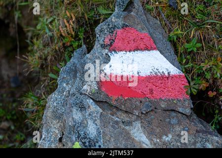 Alpenwanderweg in Österreich, markiert mit gemalter österreichischer Flagge auf einem festen Felsen entlang der Route Stockfoto