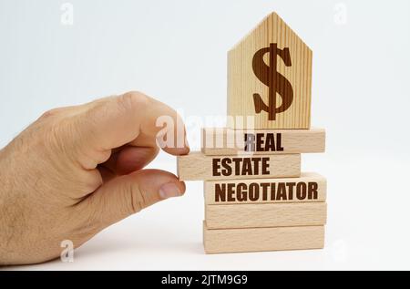 Immobilien und Geschäfte. Auf Holzblöcken mit der Aufschrift - Immobilienverhandler, gibt es ein Modell eines Hauses mit einem Dollar-Symbol. Des Mannes Stockfoto