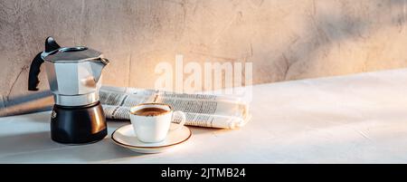 Eine Tasse Espresso, eine Kaffeemaschine und eine Zeitung in der Morgensonne Stockfoto