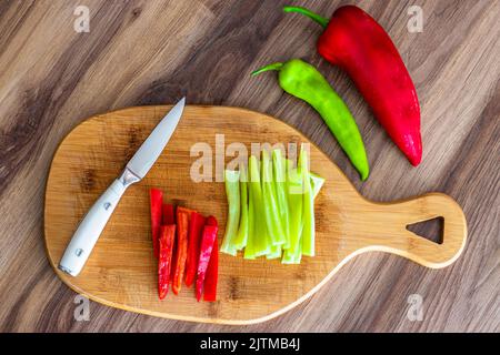 Frisches Gemüse mit Messer auf Holzhintergrund. Rote und grüne Paprika. Gemüse schneiden. Stockfoto