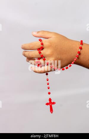 Hand eines Kindes mit einem roten Rosenkranz in der Hand in Brasilien. Stockfoto