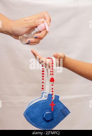 Frau, die dem Kind Gelalkohol in die Hände legt, mit Maske und einem roten Drittel zum Schutz vor dem Coronavirus in Brasilien Stockfoto