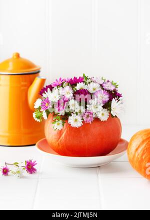 Kreatives Floristenarrangement mit bunten Asterblumen in einer Kürbisvase als Heimdeko zu Halloween oder Thanksgiving. Stockfoto