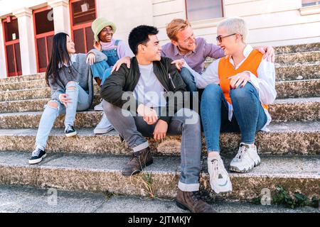 Eine Gruppe junger Leute, die lächeln und reden, sitzen auf dem Boden im Freien. Stockfoto