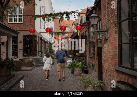 Mann und Frau, die in einer alten, dekoten Einkaufsstraße im Zentrum von Odense, Dänemark, spazieren gehen, 28. August 2022 Stockfoto