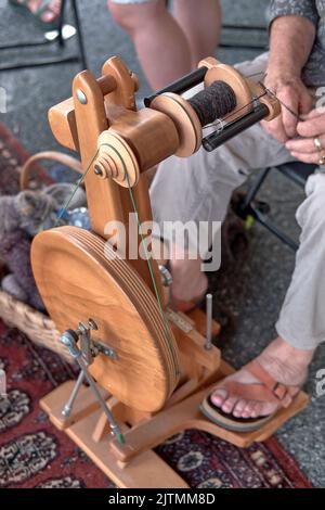 Eine Frau spinnt auf einem modernen, hölzernen Doppeltretrad im National Folk Festival Folk Life Area in Salisbury, Maryland, Wollgarn. Stockfoto