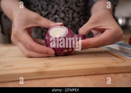 Die Hände der Frau beginnen, eine Zwiebel auf einem Holzbrett in der Küche zu schälen Stockfoto