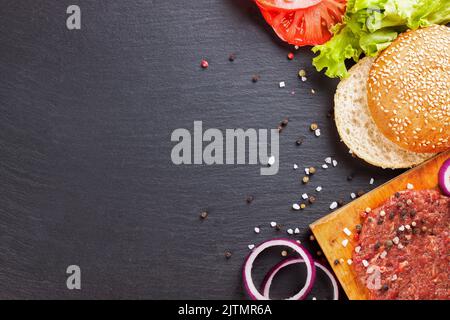 Die Zutaten für den hausgemachten Burger auf schwarzem Schieferhintergrund. Draufsicht, flach liegend mit Platz für Text. Stockfoto