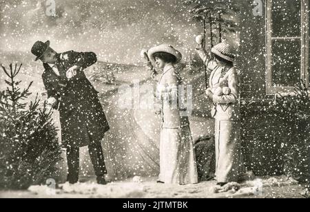 Glückliche junge Menschen, die im Schnee spielen. Vintage weihnachts-Postkarte mit Original-Kratzern und Filmkörnung Stockfoto