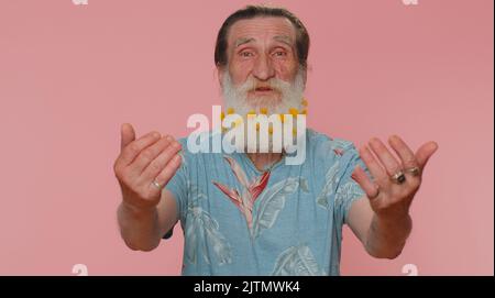 Komm zu mir, ich will dich umarmen. Älterer Mann mit Blumen im Bart spreizte die Hände und umarmte dich. Angenehmer Ausdruck, Liebesgefühle. Älterer Großvater isoliert allein auf rosafarbenem Studiohintergrund Stockfoto