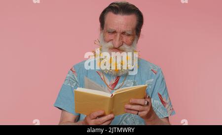 Senior Mann mit Blumen in grauhaarigen Bart lesen lustig interessante Märchen-Geschichte Buch, Freizeit Hobby, Wissen Weisheit, Bildung, Lernen, Studieren, wow. Älterer Großvater auf rosa Hintergrund Stockfoto