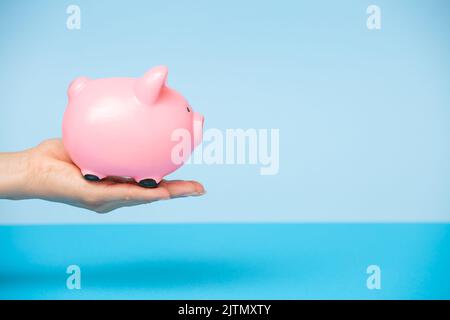 Eine Frau hält ein rosa Sparschwein auf blauem Hintergrund in der Hand.das Konzept der Investition in die Zukunft, Einsparungen, Finanzplanung.Copy space Stockfoto