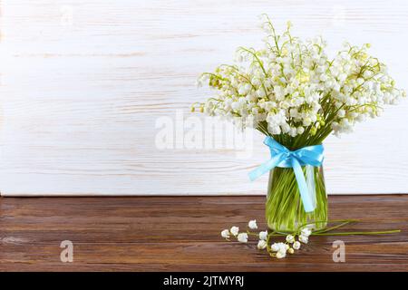 Blumenstrauß aus Lilien des Tales in einer Vase mit blauem Band auf braunem und weißem Holzhintergrund Stockfoto