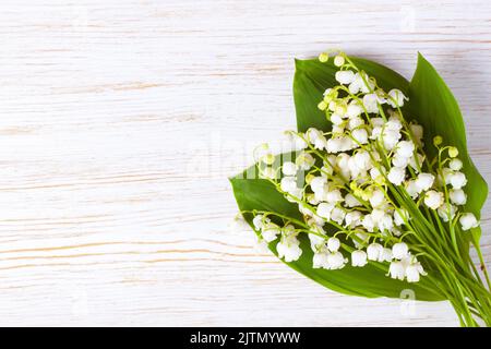 Blumenstrauß aus Lilien des Tales auf einem Vintage-weißen Holztisch. Waagerechte, flache Lage, Draufsicht. Stockfoto