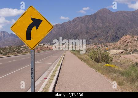 Signal zeigt Kurve in einer Straße in einer schönen Landschaft mit Bergen an einem bewölkten Tag. Stockfoto