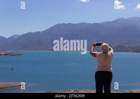 Blonde Frau, die an einem bewölkten Tag ein Foto in einer wunderschönen Landschaft mit einem See und Bergen gemacht hat. Stockfoto