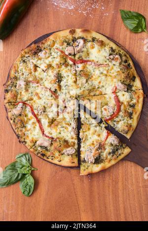 Hähnchenpizza auf einem Holztablett serviert und in acht Stücke geschnitten. Tomaten- und Basilikumsoße. Stockfoto