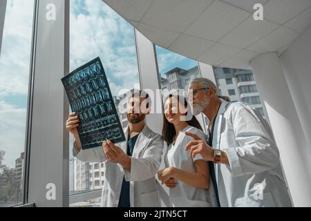 Arztkollegen schauen sich die Röntgen- oder MRT-Untersuchung der Wirbelsäule des Patienten in der Medizinklinik an und diskutieren sie Stockfoto