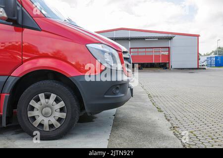 Vorderteil eines roten Lieferwagens vor dem Logistiklagerzentrum - moderner Transport von Waren zu Kunden Stockfoto