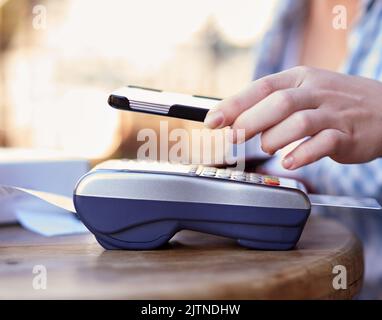 Bezahlen ist so einfach wie 1,2,3. Eine nicht identifizierbare Frau, die eine mobile Zahlung mit ihrem Smartphone und einem Kartenautomaten in einem Café macht. Stockfoto