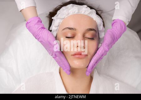 Gesichtsmassage Schönheitsbehandlung. Nahaufnahme einer jungen Frau, das Gesicht auf dem Rücken liegend, Gesichtsstraffung Massage bekommen, Stockfoto