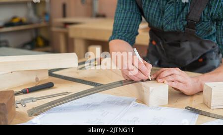 Ein Zimmermann mißt Holzbohlen und macht in einer Werkstatt mit einem Bleistift Markierungen. Stockfoto