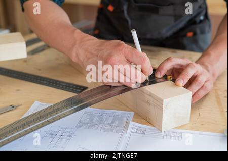 Ein Zimmermann mißt Holzbohlen und macht in einer Werkstatt mit einem Bleistift Markierungen. Stockfoto