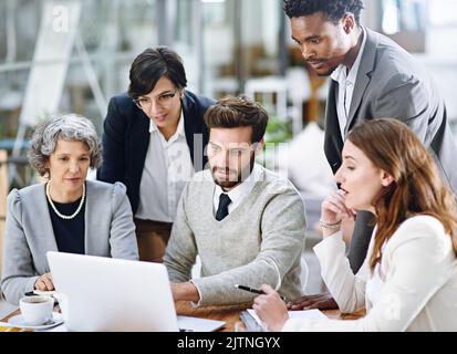 Die Bewältigung ihrer Herausforderungen mit Hilfe von Technologie. Eine Gruppe von Geschäftsleuten, die in einem Büro an einem Laptop arbeiten. Stockfoto