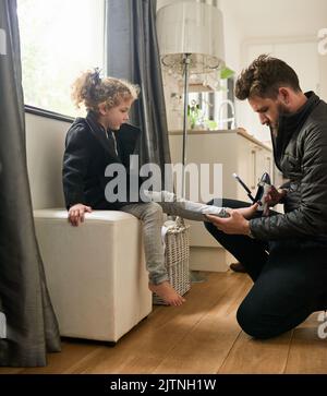 Vater wird immer da sein, um ihr zu helfen. Ein Vater, der seiner Tochter hilft, zieht zu Hause ihre Schuhe an. Stockfoto