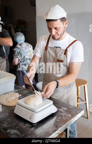 Der Prozess der Brotherstellung. Den Weizenteig in Stücke teilen. Vertikales Foto. Stockfoto