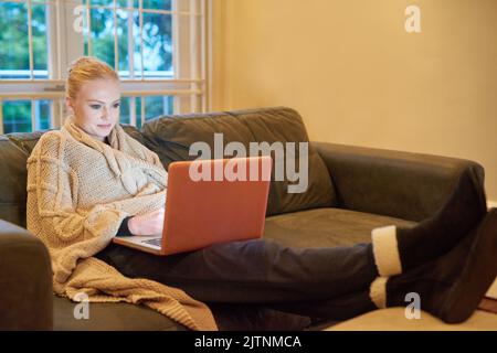Wer braucht ein Kino. Eine attraktive junge Frau, die sich zu Hause einen Film auf ihrem Laptop ansieht. Stockfoto