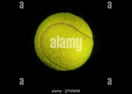 Unscharfer, gelber Tennisball, der in Nahaufnahme vor einem dunkelschwarzen Hintergrund fotografiert wurde Stockfoto