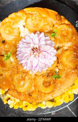 Hausgemachter umgedrehter Ananaskuchen mit Minze und dekorativen essbaren Blumen. Stockfoto