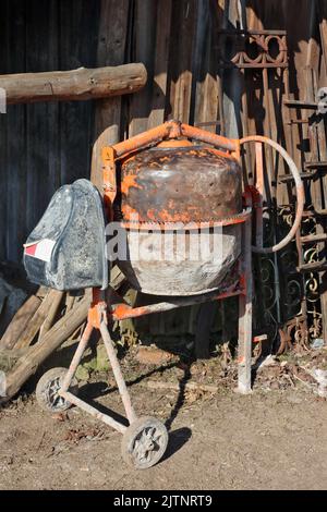 Kleiner alter Betonmischer in der Nähe des Holzschuppens Stockfoto