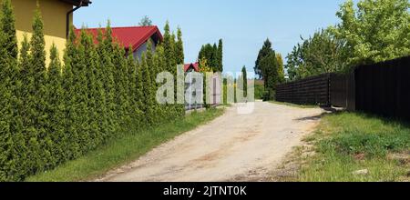 An den Rändern der Dorfstraße gibt es Zäune und grüne Hecken. Stockfoto