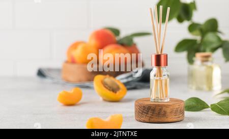 Innenparfüm mit dem Duft von Aprikosen. Glas mit Aromaöl und Banbu-Sticks Stockfoto