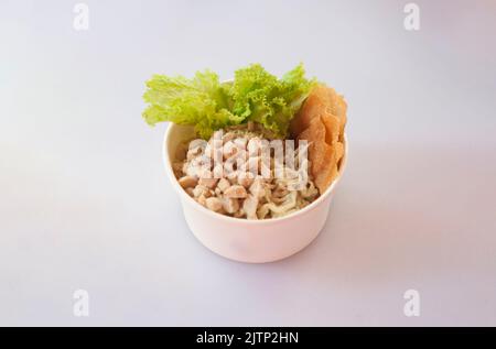 Mie Ayam oder Hühnernudel auf weißem Hintergrund. Gelbe Weizennudeln mit Hühnerfleisch-Belag, serviert mit gebratenen Knödeln, Stockfoto