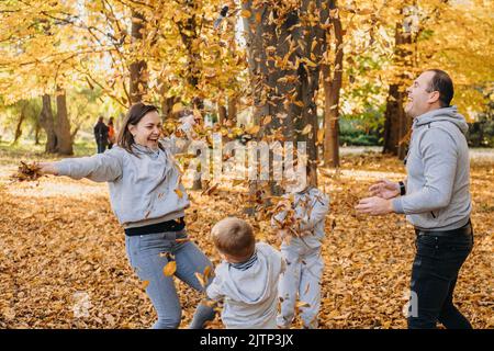 Porträt einer Familie mit Kindern, die im Herbst Herbstblätter im Park werfen. Familienportrait von vier Mitgliedern, Vater, Mutter und Kindern. Familie Stockfoto