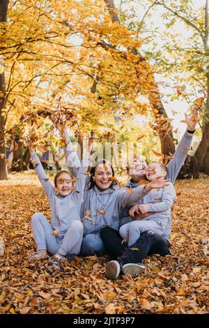 Porträt einer Familie, die Gruppenfotos macht, während sie im Herbst gerne trockene Blätter in verschiedenen Farben in die Luft wirft und Zeit miteinander verbringt Stockfoto