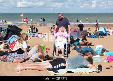 Alte Dame im Rollstuhl, die mit der Familie am Sandstrand in Botany Bay kent sonnenbaden geht Stockfoto