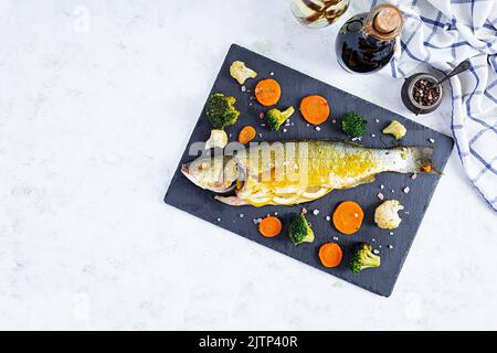 Gebackener Seebarsch mit Gemüse und Gemüse auf Steinplatte Stockfoto