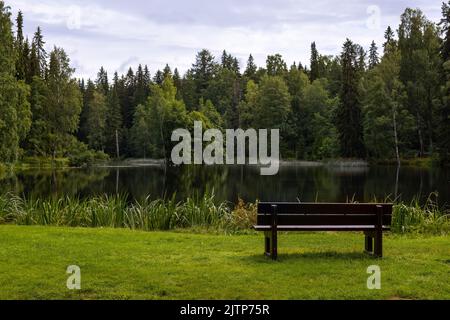 Parkbank neben einem ruhigen Teich im Park in Finnland Stockfoto