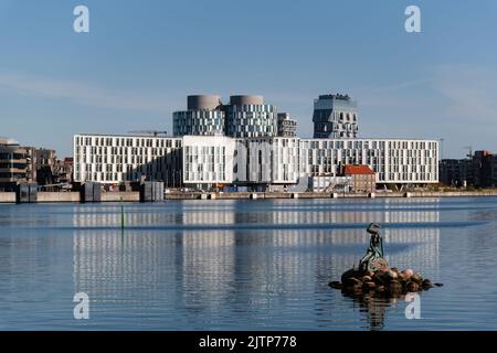 Kopenhagen, Dänemark. 13. August 2022. Gentechnisch veränderte kleine Meerjungfrau-Skulptur mit UN City-Gebäuden im Hintergrund. Stockfoto