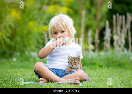 Cute blonde Kleinkind Kind, süßen Jungen, spielen im Garten mit kleinen Kätzchen, Buch lesen Stockfoto