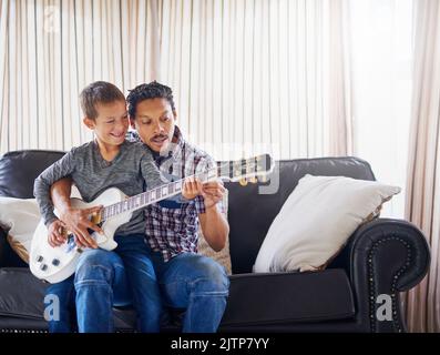 Seinem Sohn eine neue Melodie beibringen. Ein Vater lehrt seinem Sohn, wie er zu Hause Gitarre spielen kann. Stockfoto